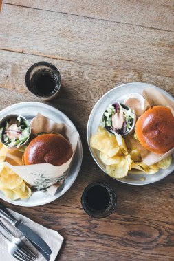 Ahşap bir masada cips ve salata ile bir tabak tabaktabak tabaktabak sebze ile Craft sığır burger.