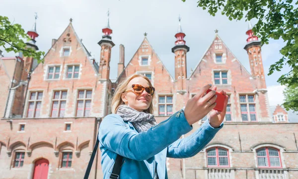 벨기에 브뤼헤에서 휴대폰으로 셀카를 찍는 세련된 젊은 여성 관광객. — 스톡 사진