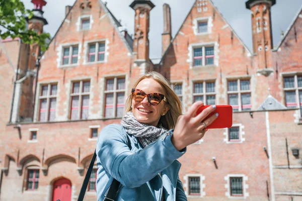 벨기에 브뤼헤에서 휴대폰으로 셀카를 찍는 세련된 젊은 여성 관광객. — 스톡 사진