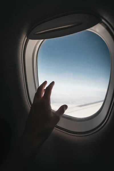 Porthole window in the plane with a mans hand during the flight.