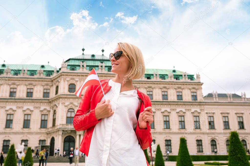 Female traveler with the flag of Austria against the backdrop of the Upper Belvedere Palace in Vienna.