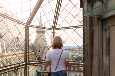 A woman admires the panorama of Vienna from the viewpoint of St. Stephens Cathedral and holds the flag of Austria in her hands. clipart
