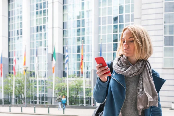 A young woman stands with a telephone in her hands opposite the European Parliament building in Brussels, Belgium.