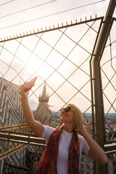Uma mulher tira uma foto selfie em seu telefone no telhado da Catedral de St. Stephens em Viena, Áustria — Fotografia de Stock