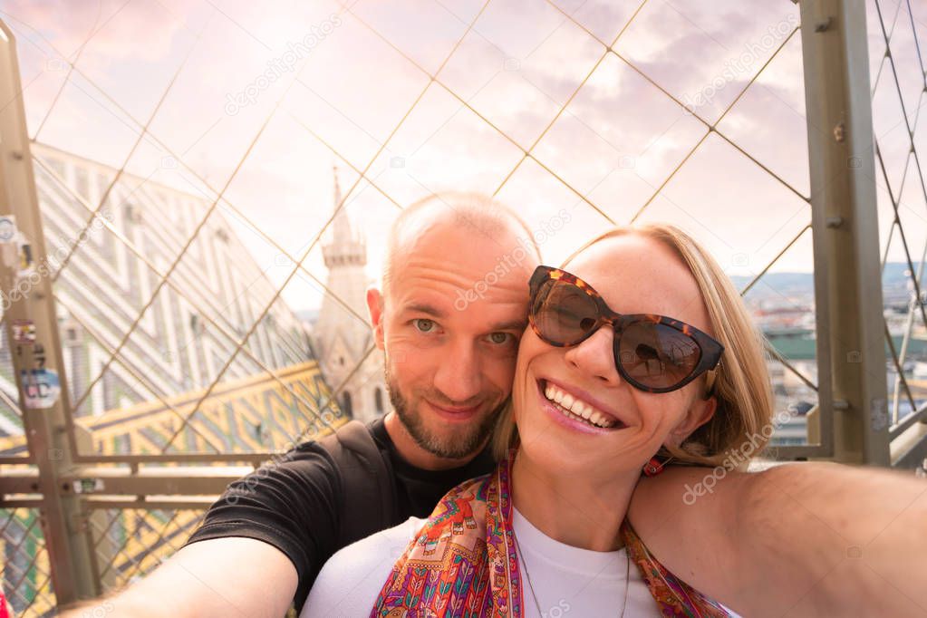 Young couple taking a selfie against the backdrop of the city panorama at sunset from the North Tower of St. Stephens Cathedral in Vienna, Austria