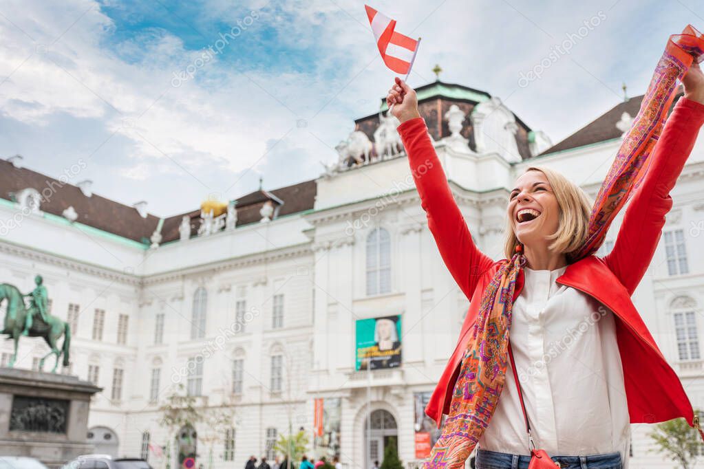 Woman tourist stands against the backdrop of the Austrian National Library in Vienna with raised arms and the flag of Austria, Vienna