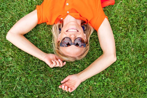 Вид сверху на молодую женщину, лежащую на траве и мило улыбающуюся . — стоковое фото