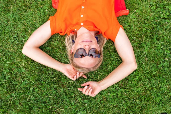 Horní pohled na mladou ženu ležící na trávě a usmívající se roztomilý. — Stock fotografie