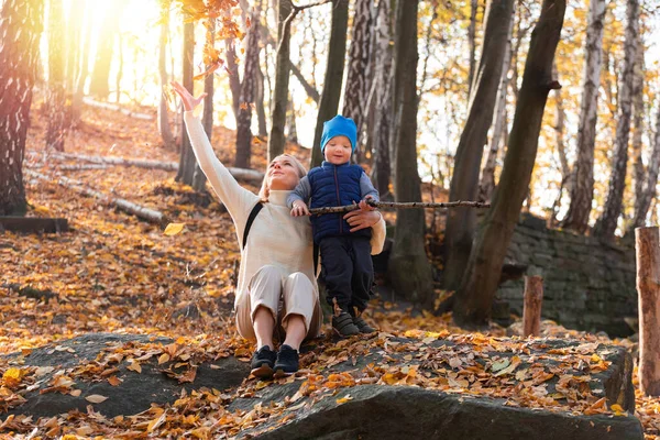 Menino e sua mãe estão sentados na floresta de outono e jogando folhas. — Fotografia de Stock