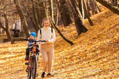 Mutlu anne, sonbahar parkında arkada bağlı bir çocukla bisiklete biniyor..