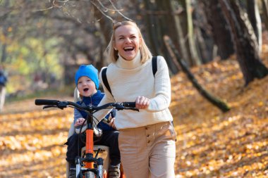 Mutlu anne, sonbahar parkında arkada bağlı bir çocukla bisiklete biniyor..