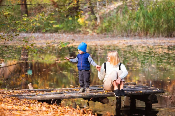 Šťastná mladá matka a její syn tráví čas v podzimním parku u rybníka. — Stock fotografie