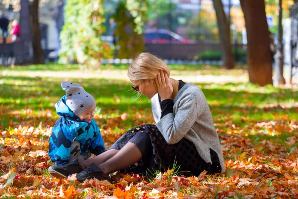 Mãe e filho são jogados nas folhas caídas para um passeio no parque da cidade — Fotografia de Stock