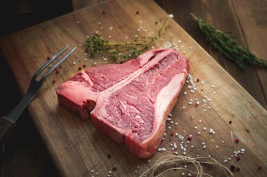 raw t bone steak of beef on the butcher's Board with pepper, salt, herbs, close twine clipart