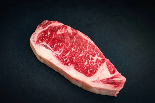 Свіжий мармуровий яловичий стрічковий стейк на чорному тлі — стокове фото