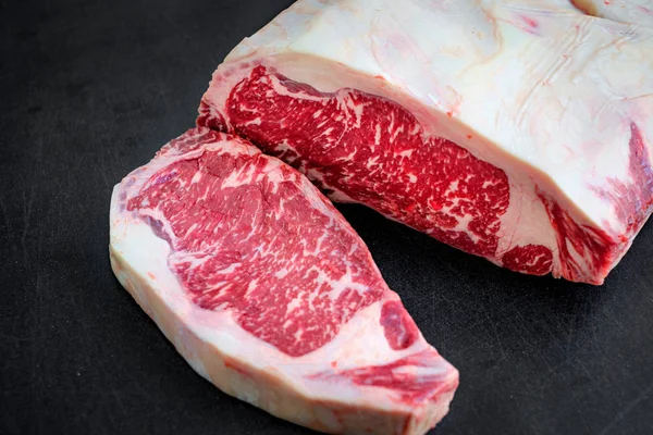Groot stuk van de ruwe rundvlees strip loin biefstuk op een zwarte achtergrond — Stockfoto