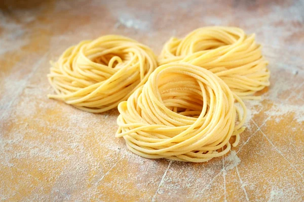 Raw homemade spaghetti nest with flour on a wooden table. fresh — Stock Photo, Image