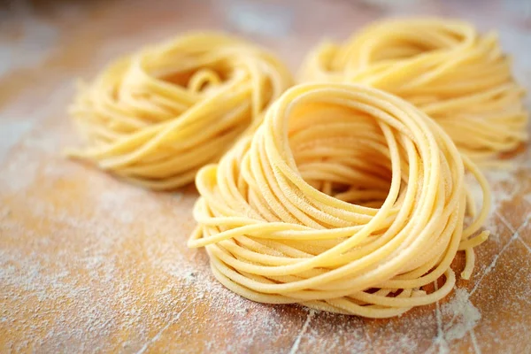 Raw homemade spaghetti nest with flour on a wooden table. fresh — Stock Photo, Image