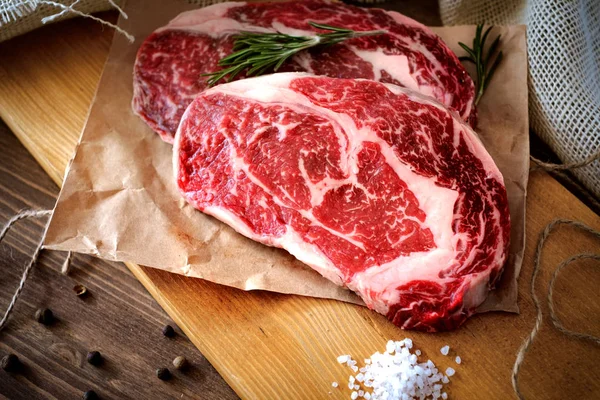 Two raw rib eye steak on a wooden Board on a table prepared for — Stock Photo, Image