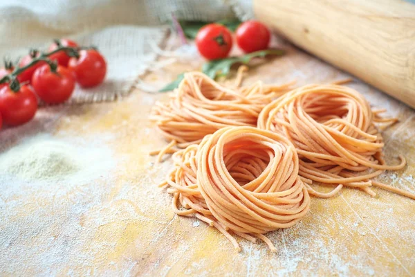 Raw homemade colored spaghetti nest with flour on a wooden table — Stock Photo, Image