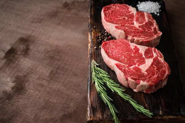 Zwei frische rohe Rib-Eye-Steaks auf Holzbrett auf Holzgrund — Stockfoto