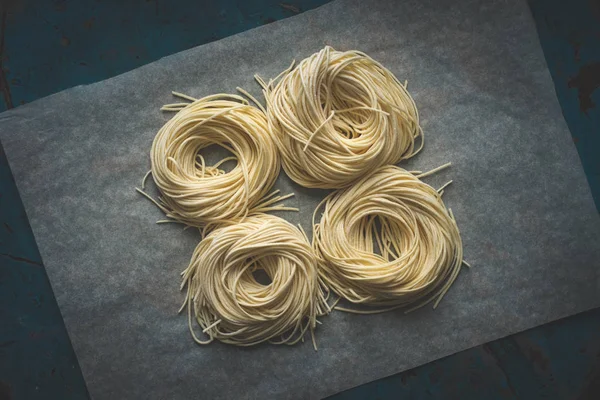 Гнізда свіжого спагеті на папері на темному фоні — стокове фото