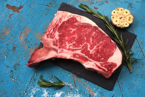 Surový klubový steak na kamenné desce na modrém dřevěném pozadí — Stock fotografie