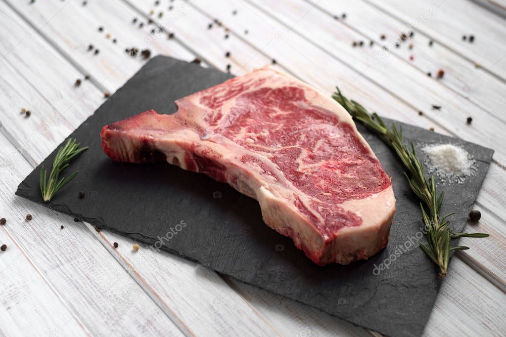 raw club steak on a stone Board on white wooden background