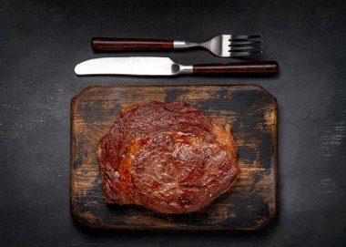 Sulu ızgara kaburga gözü bifteği ve çıtır çıtır ekmek ve çatalla ahşap üzerinde yenmeye hazır.