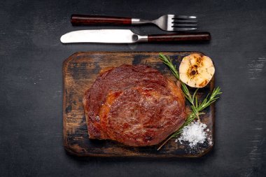 Ahşap bir tahtanın üzerinde ızgara biftek, et tabakları servis ediliyor.