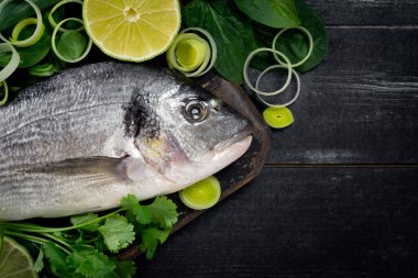 Siyah ahşap zemin üzerinde limon ve bitkilerle taze ve çiğ dorada balığı, üst görünüm ve boşluk kopyala