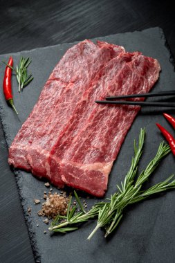 Koyu arkaplanda taş bir tahtada ızgara yaptığı için çiğ mermer sığır eti parçaları. Yakiniku üst görünümü için et