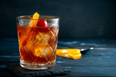 Viski kokteyli, bir dilim portakal, kiraz ve buz, koyu arka planda klasik bir alkollü içecek.