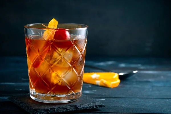 Viski kokteyli, bir dilim portakal, kiraz ve buz, koyu arka planda klasik bir alkollü içecek.