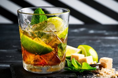 Viski ve kola kokteyli limon, nane, esmer şeker ve buz, koyu ahşap arka planda bir bardakta alkollü içecek, kopyalama alanı.