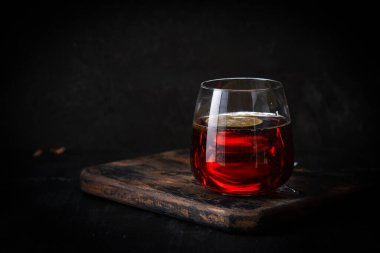 Bardakta sıcak çay, ahşap tahtada limon, koyu arka planda.