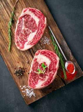 Izgara için ahşap bir tahtada biber ve tuzla tatlandırılmış mermer biftekten iki çiğ kaburga bifteği.
