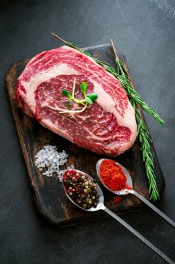 Baharatlı mermer çiğ Ribeye bifteği ve kesim tahtasında kırmızı biber, gri arka plan, üst manzara.