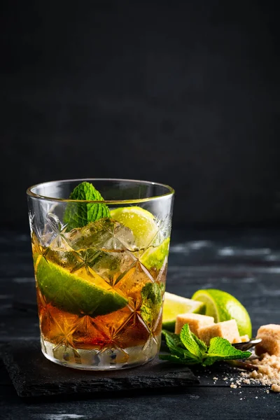 Viski ve kola kokteyli, limon, nane ve buz, koyu ahşap arka planda bir bardakta alkollü içecek, kopyalama alanı.