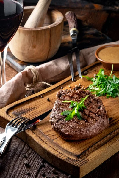 Grilled chuck beef steak with wine, knife and fork on a wooden Board. Whole roast piece of meat, rustic style