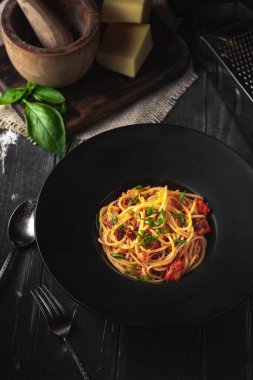 Geleneksel kurutulmuş domatesli spagetti bolonezi. Siyah ahşap arka planda siyah tabakta domates soslu İtalyan makarnası.