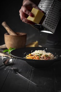 Elleri rendelenmiş parmesan peyniri makarna içinde kurutulmuş domates ve siyah bir tabakta siyah ahşap arka planda sos..