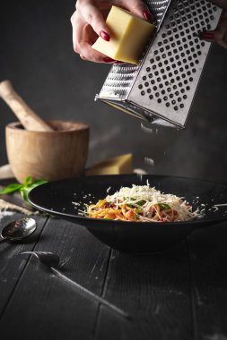 Elleri rendelenmiş parmesan peyniri makarna içinde kurutulmuş domates ve siyah bir tabakta siyah ahşap arka planda sos..