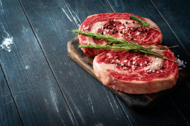 Ahşap bir tahtada iki taze biftek ve siyah bir arka planda tuz ve biber. Izgara için çiğ kaburga kavramı, kapat ve boşluğu kopyala