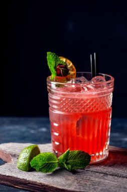 Bir bardak buzlu, naneli ve limonlu kırmızı alkollü kokteyl. Karanlık bir arka planda yaz ferahlatıcı içeceği