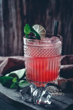 Bir bardak buzlu, naneli ve limonlu kırmızı alkollü kokteyl. Karanlık bir arka planda yaz ferahlatıcı içeceği