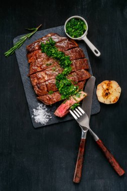 Tahtaya sarımsak ve sosla dilimlenmiş siyah Angus bifteği yemeye hazır. Koyu siyah ahşap arka planda akşam yemeği için hazır yemek. Kopyalama alanı olan üst görünüm