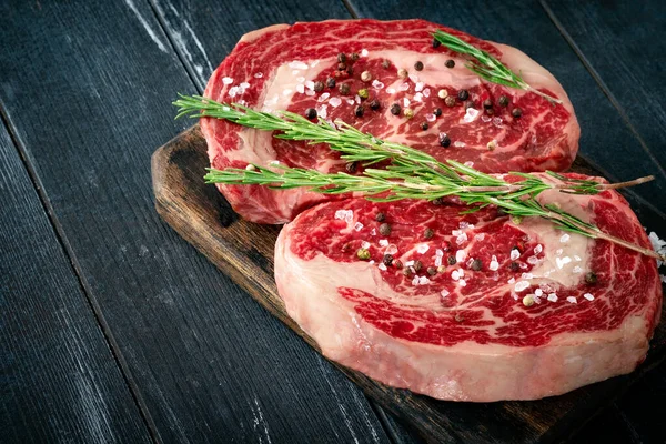 濃い目の背景に塩とコショウで板に2つの新鮮な牛肉ステーキ グリル用のコンセプト生リブの目を閉じます — ストック写真