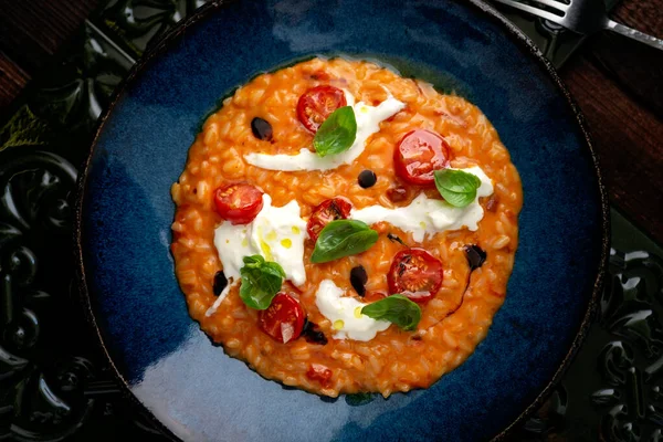 Mavi tabakta domatesli, fesleğenli, peynirli ve zeytinyağlı risotto. İtalyan ulusal mutfağı, köy usulü, yakın plan.