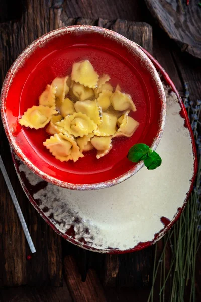 传统的意大利多特利尼在一个木制桌子上的红色碗里的肉汤里 素食汤顶视图 乡村风格 — 图库照片